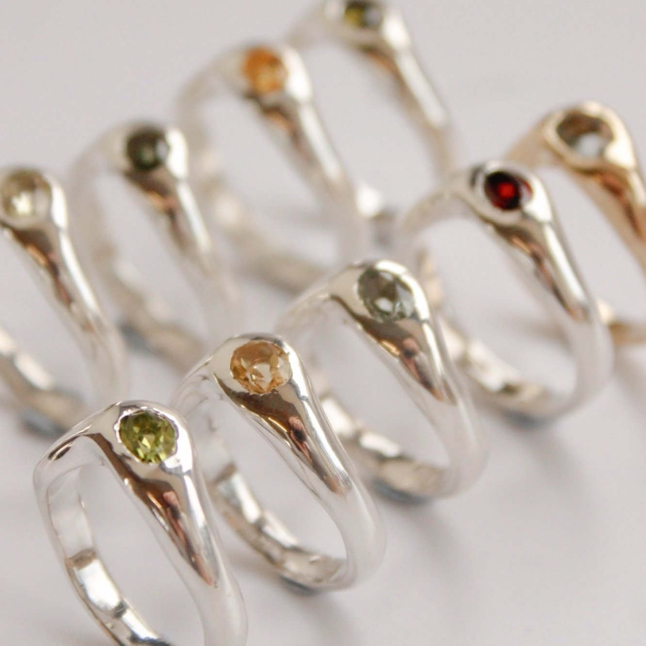 The Silk ring (Copy) is a sterling silver ring set with a colorful gemstone—green, yellow, or red—displayed among other vibrant rings in neat rows on a white surface.