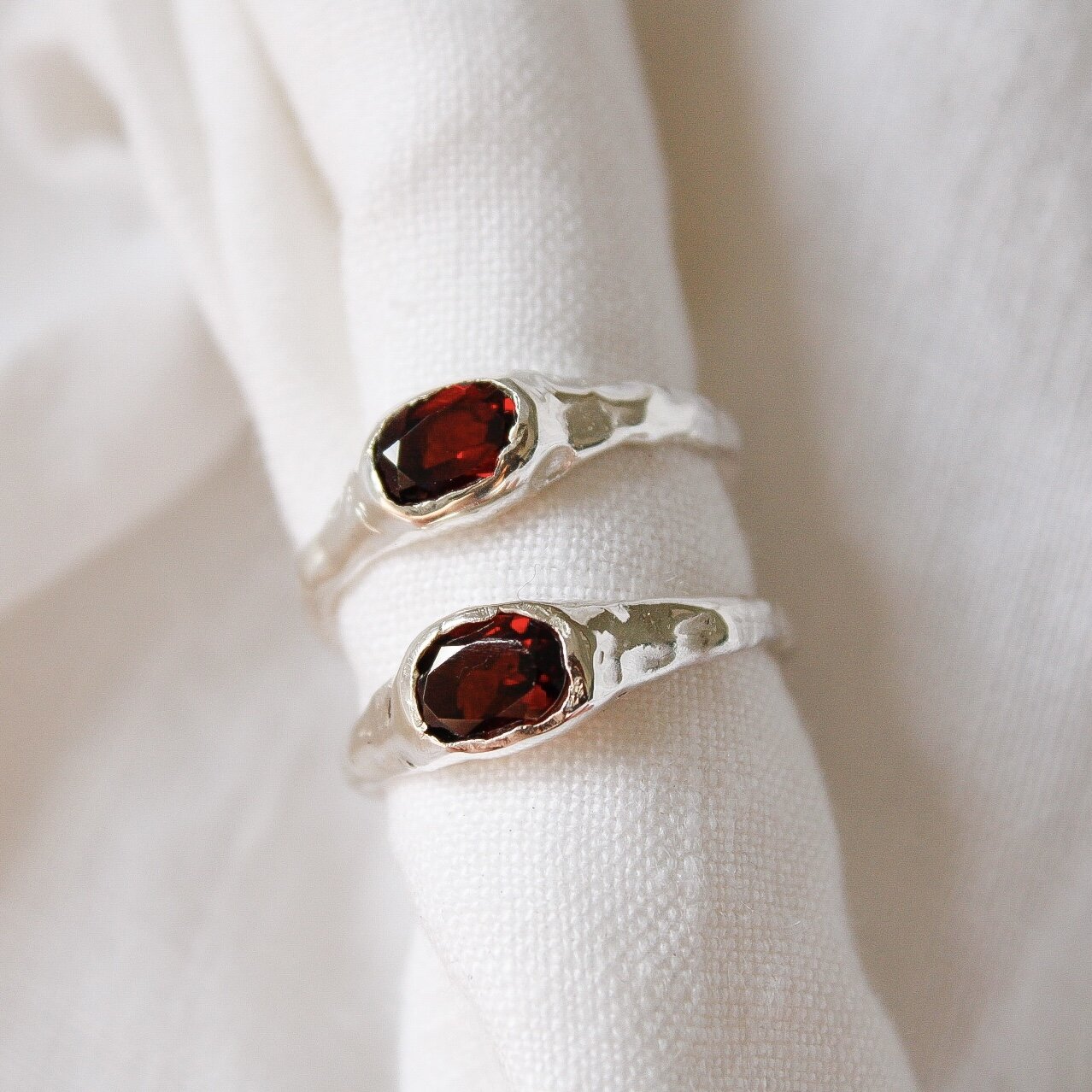 The Florence ring features hammered sterling silver and an oval deep red gemstone, beautifully displayed on soft white fabric—perfect as a bespoke or statement ring for any occasion.