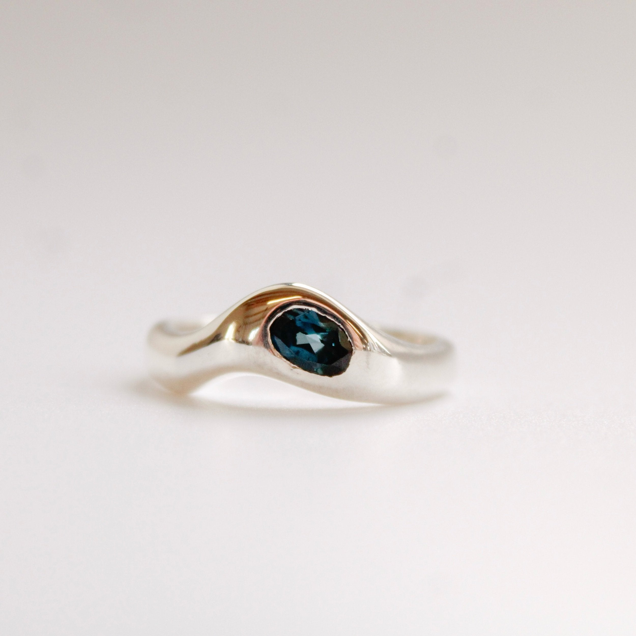 The Silk ring (Copy) is a handmade silver ring with a wavy, modern design and an oval dark blue gemstone set at the center, shown against a plain white background.