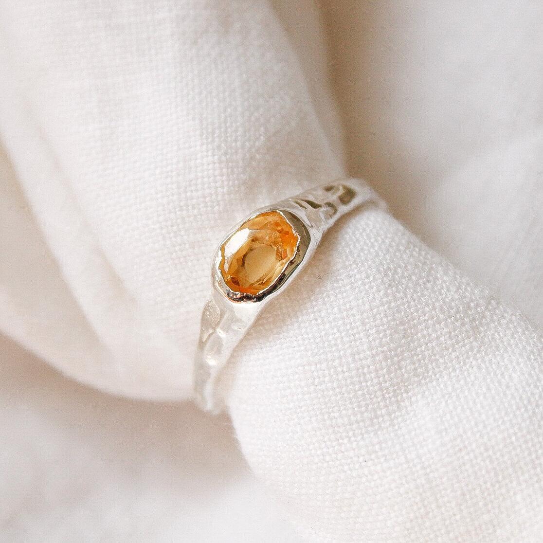The Florence ring, a textured sterling silver statement piece with an oval yellow gemstone, shown close-up against a soft white fabric background.