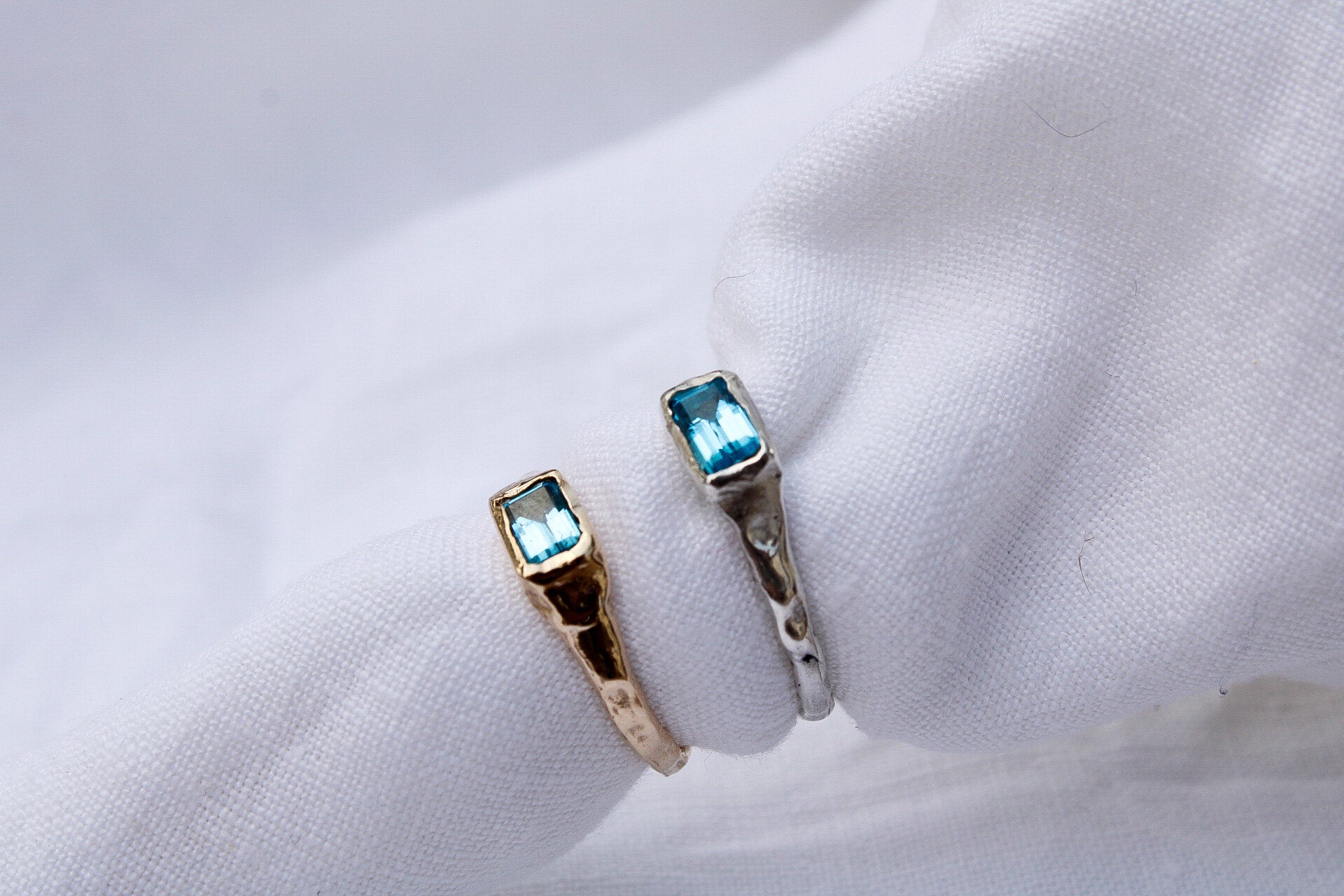The Pool ring, crafted from recycled sterling silver and gold, features a rectangular blue gemstone. Both handmade rings are displayed on a white fabric background.