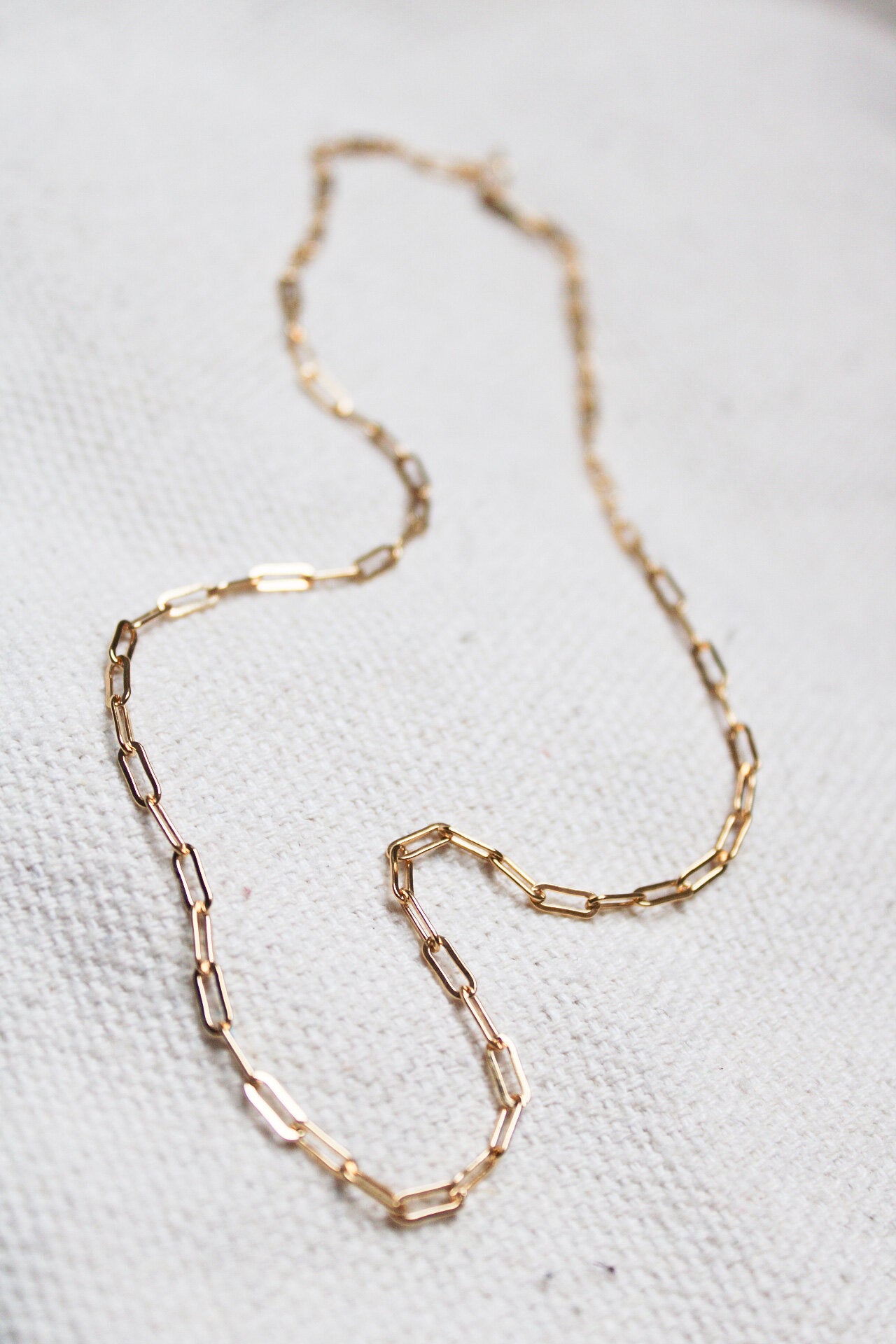The Gold linked chain, featuring delicate elongated rectangular links, is displayed on a textured white fabric—an elegant choice for everyday wear.