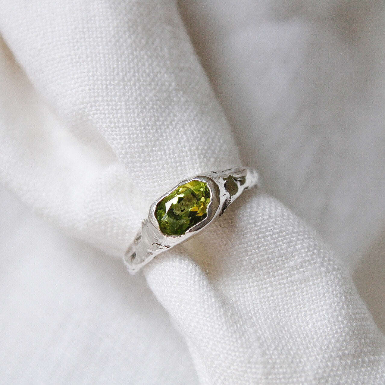 The Florence ring, crafted in sterling silver with an oval green gemstone, is displayed on white textured fabric, creating a striking statement piece.