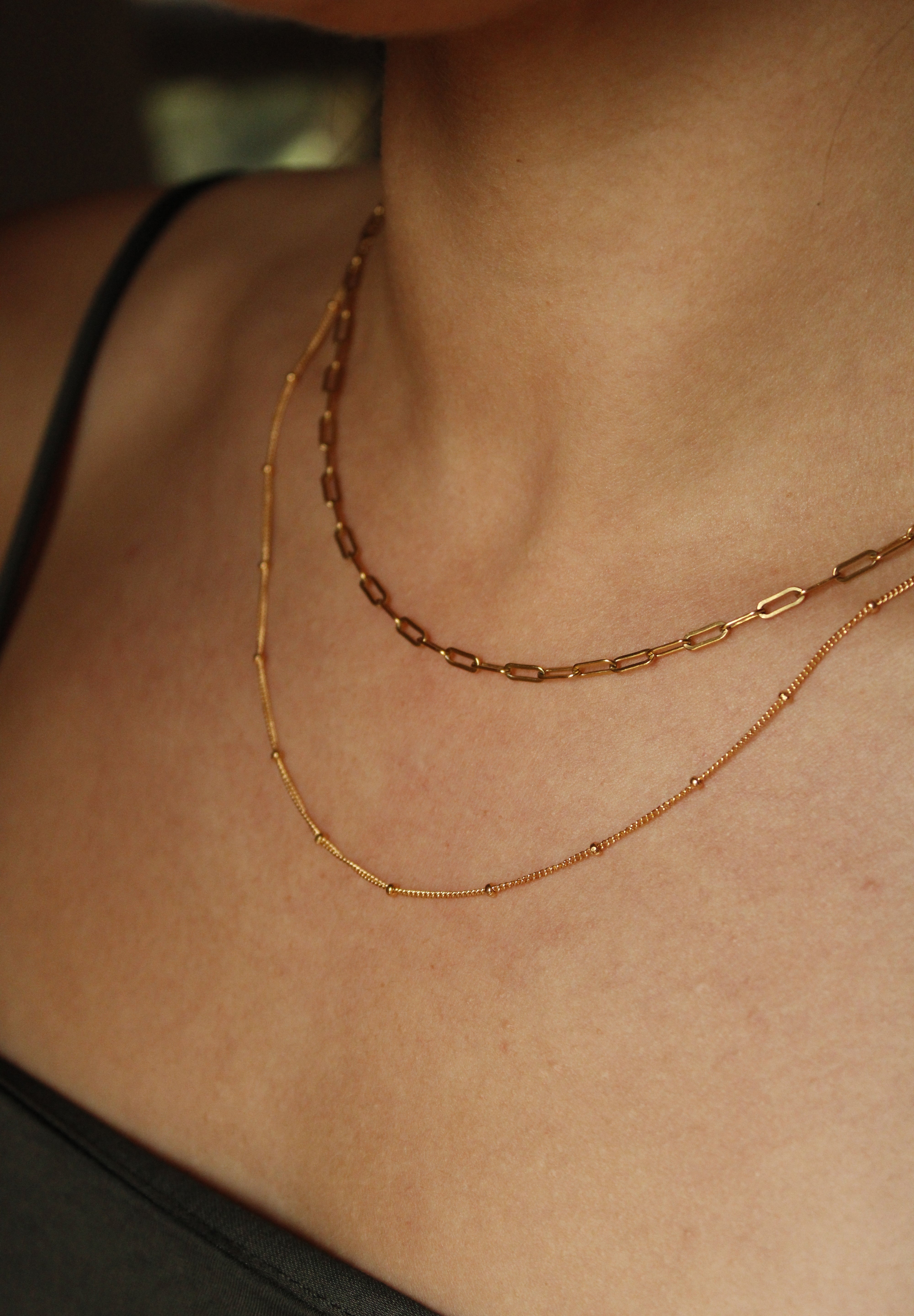 A close-up of a person’s neck wearing two gold filled necklaces—one a delicate chain, the other the Gold linked chain with larger, oval links. The dark thin-strap top highlights this perfect everyday necklace combo.