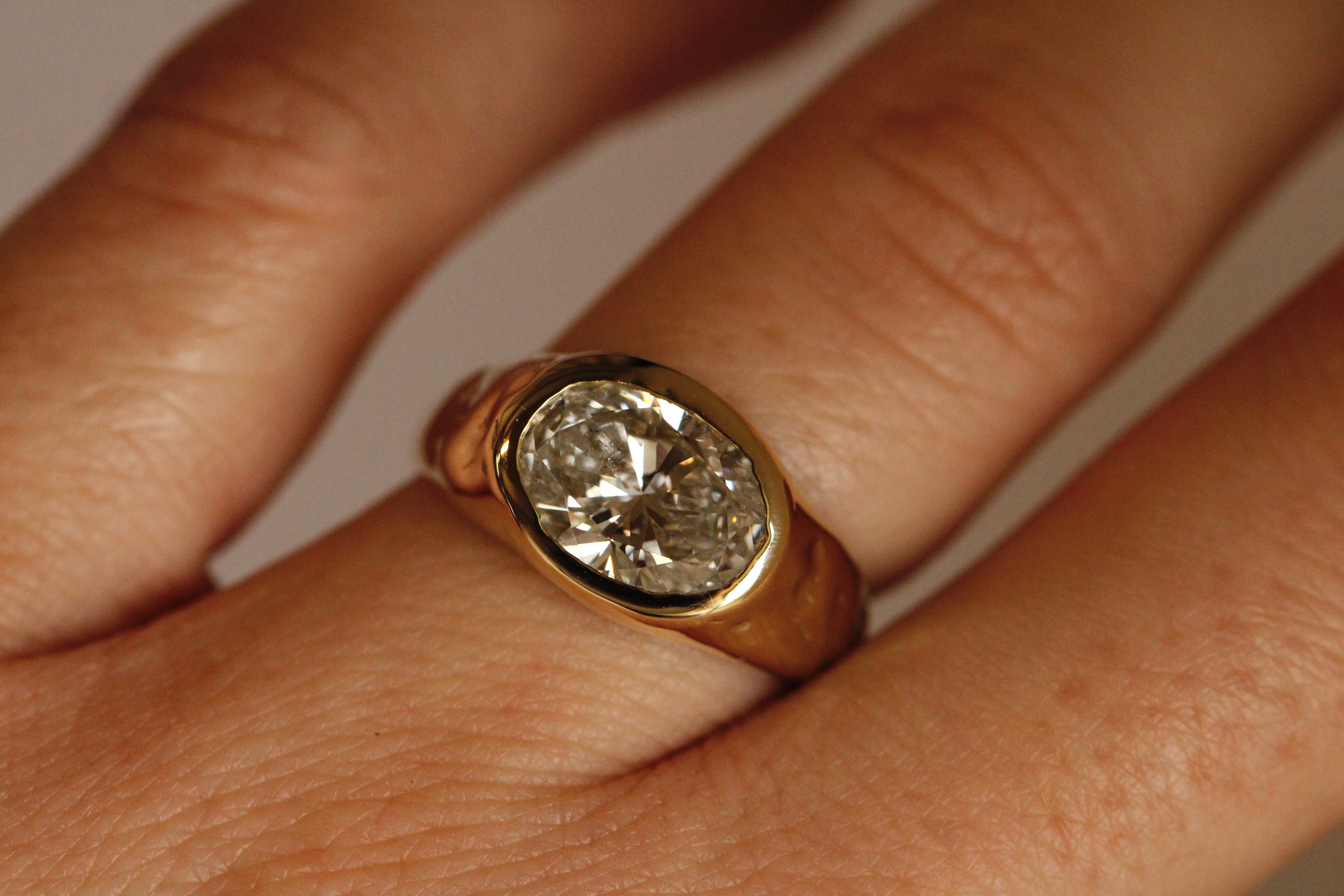 Gold ring with a diamond on a finger against a neutral background