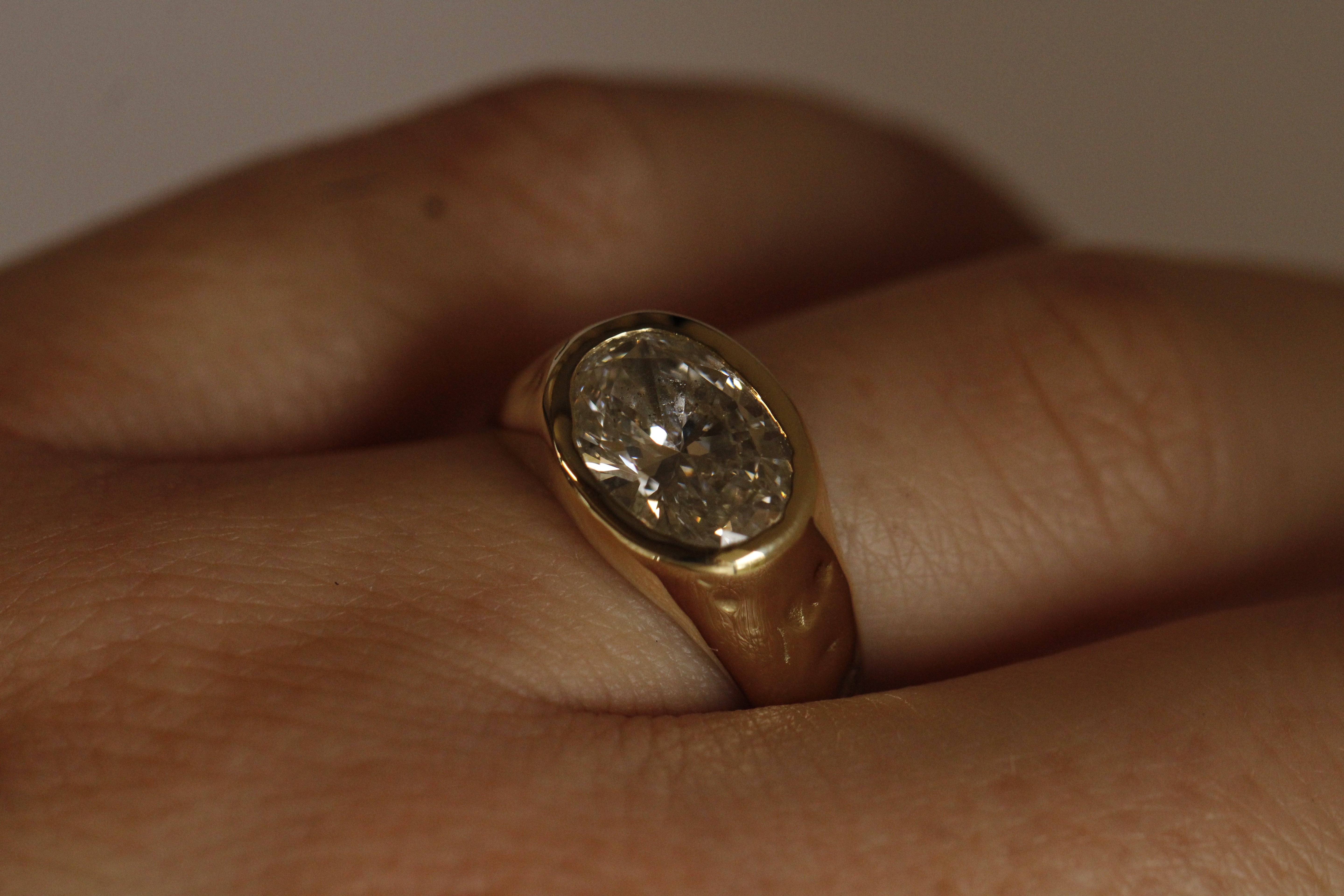 Gold ring with a diamond on a finger against a neutral background