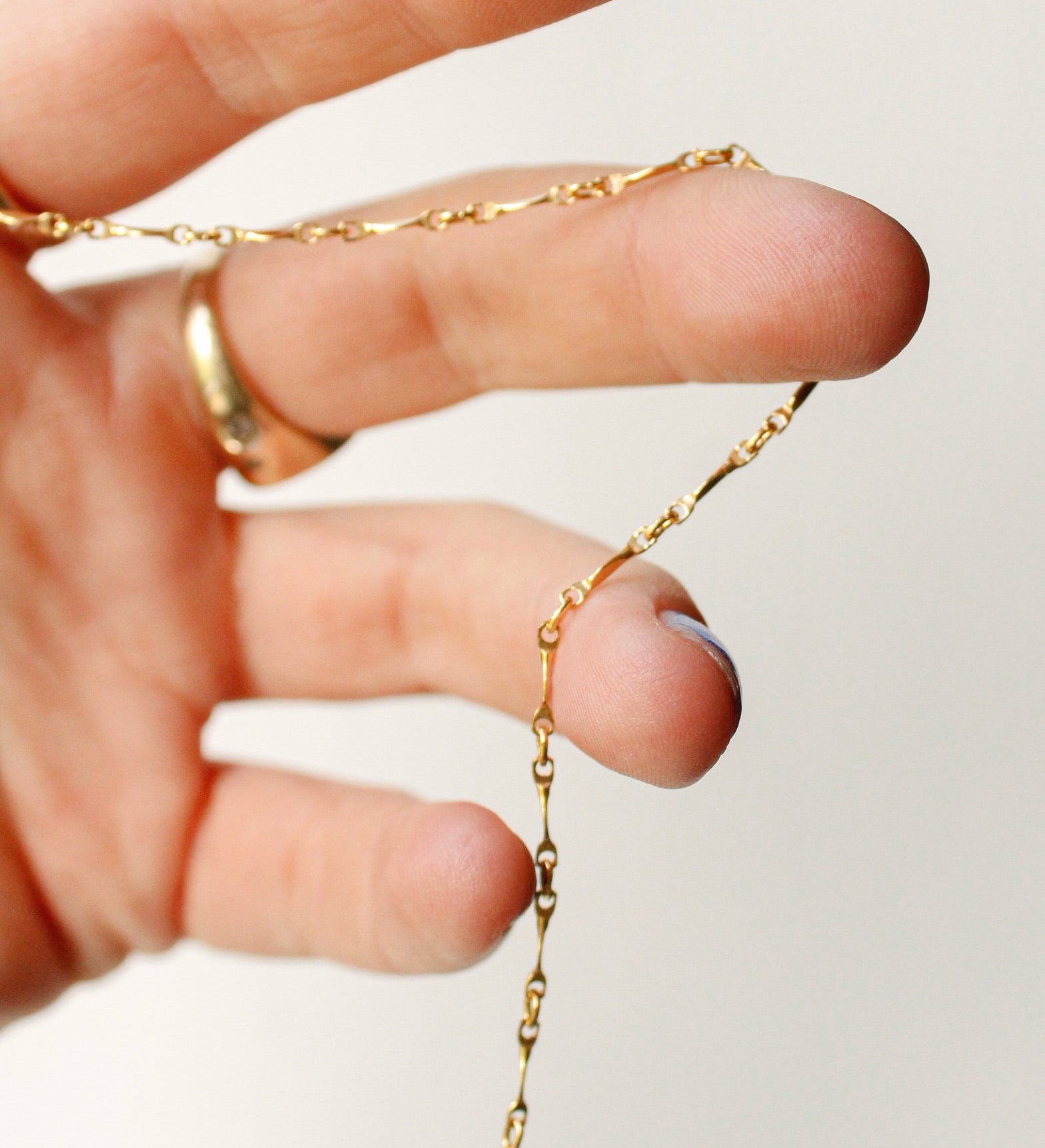 A close-up of a hand holding the Twisted link necklace—a delicate gold filled chain—while a gold ring glimmers on the ring finger. The plain, light background highlights the minimalist design of this elegant necklace.