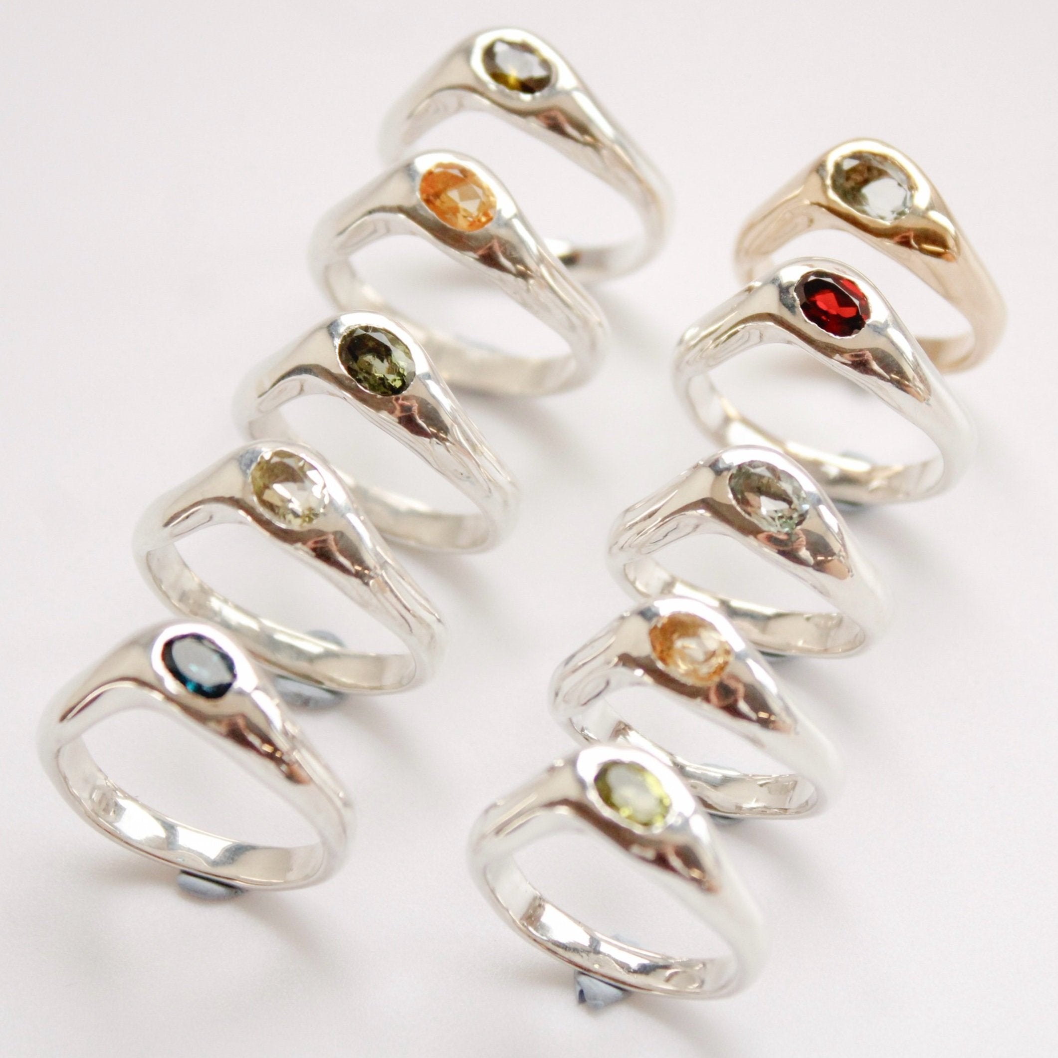 The Silk ring: a collection of ten sterling silver rings, each featuring a unique colored gemstone, displayed in two rows on a white background.