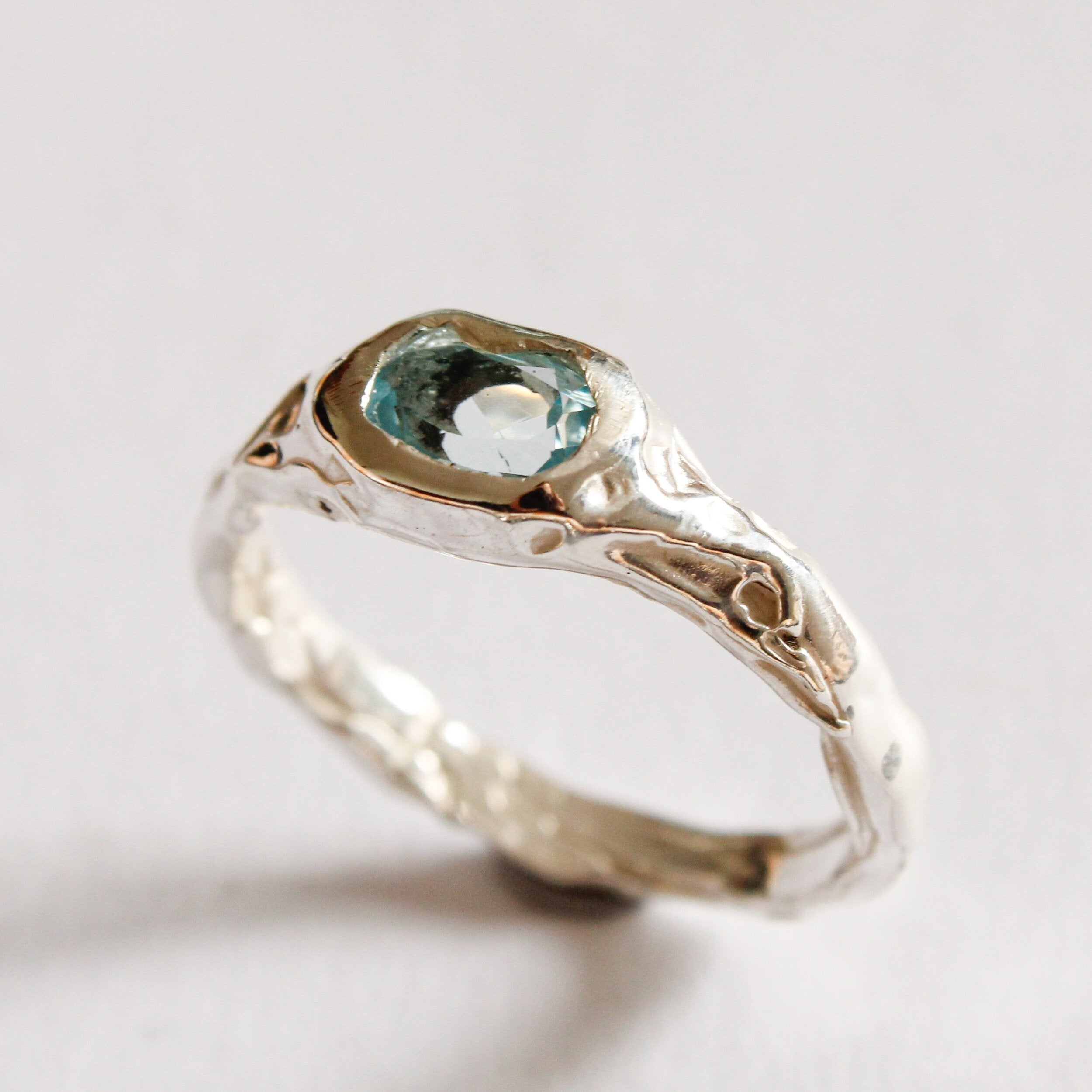 The Florence ring is a sterling silver statement piece with a textured, organic band and an oval light blue gemstone at the center, shown against a simple light background.