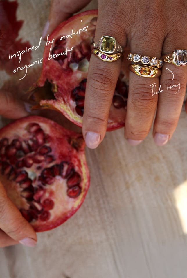 Hand holding a pomegranate with gold rings on a wooden surface