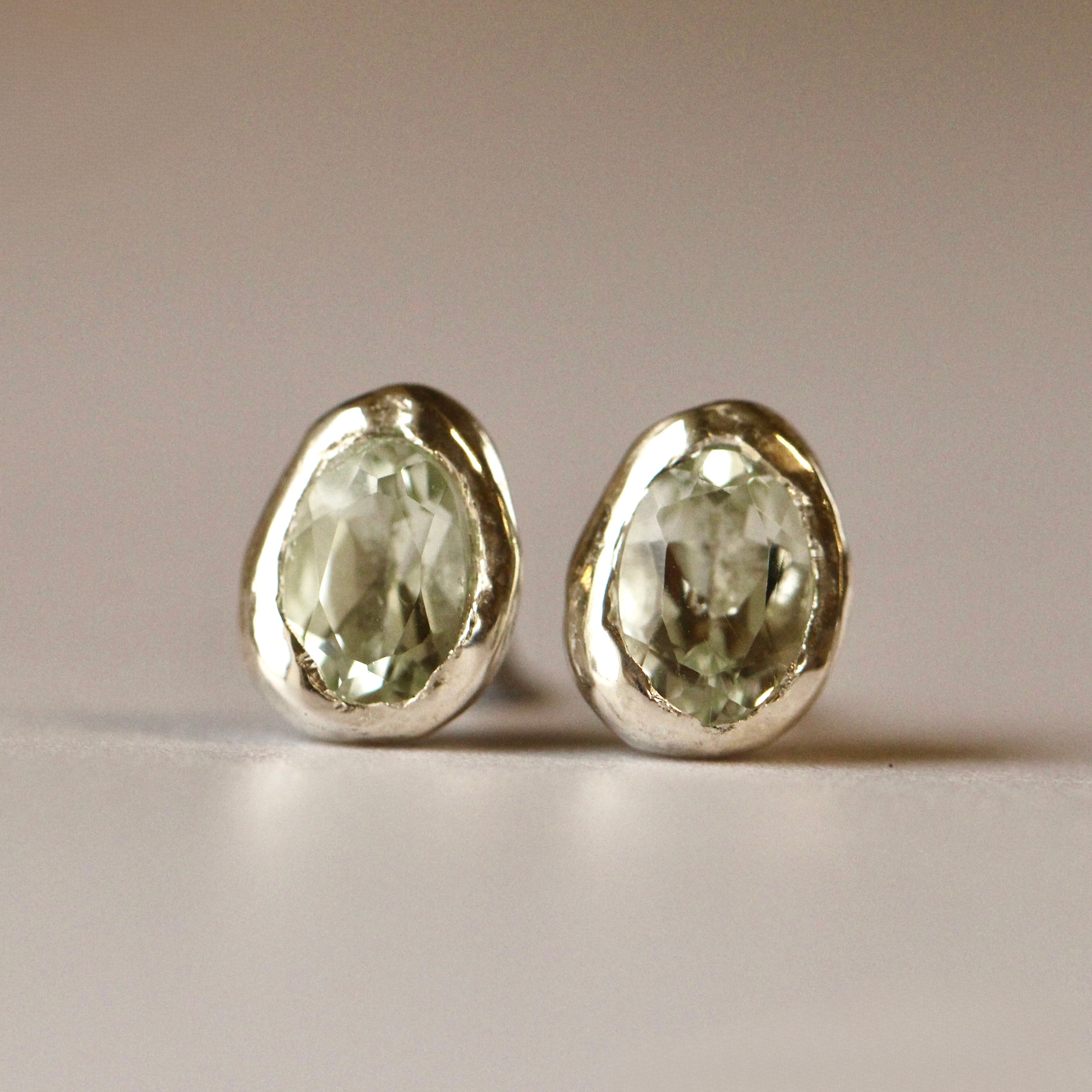 Pair of silver earrings with green gemstones on a neutral background