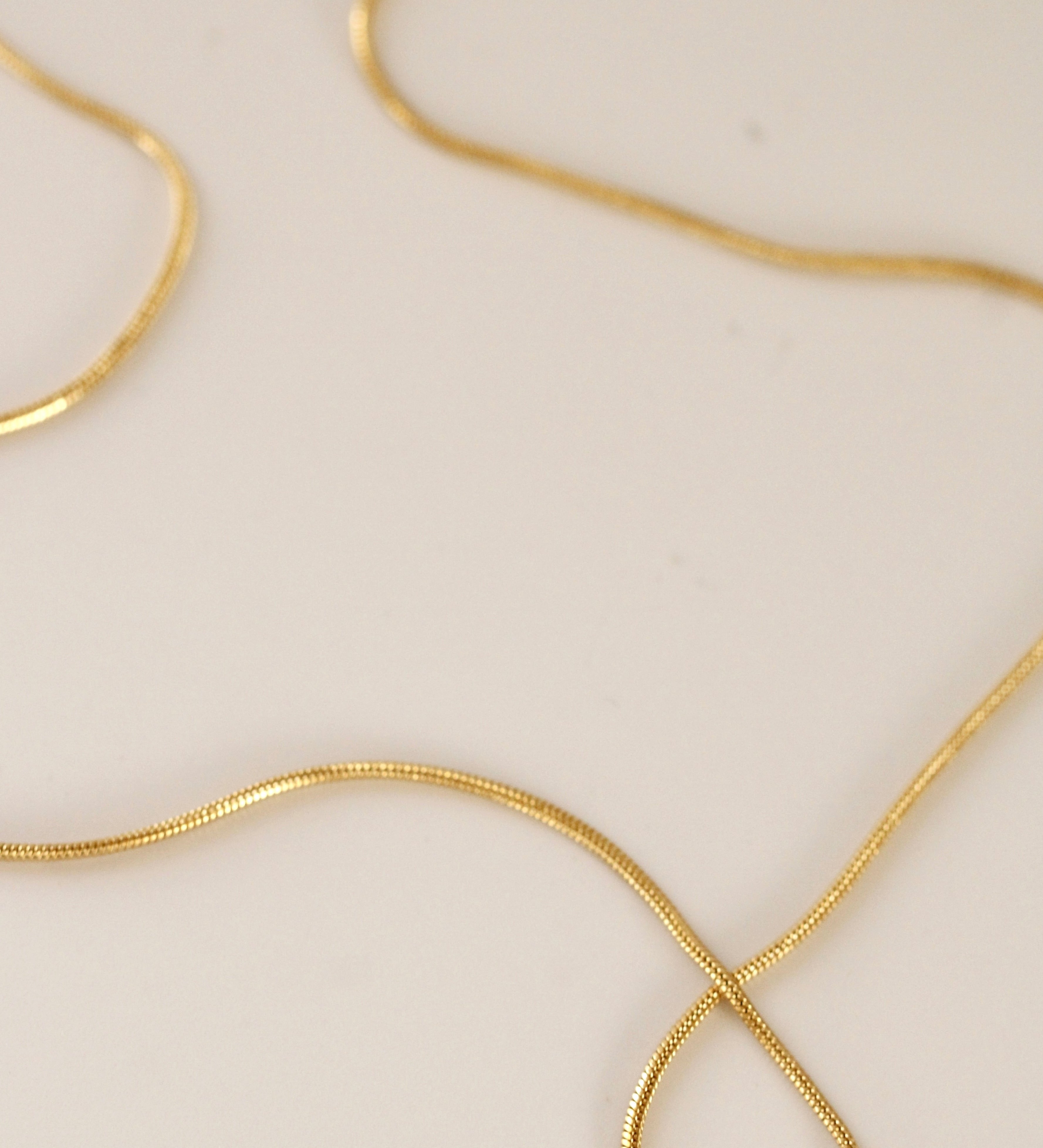 The Trail chain necklace, crafted in gold filled material, lies in gentle curves on a smooth surface—an ideal minimalist piece for everyday wear.