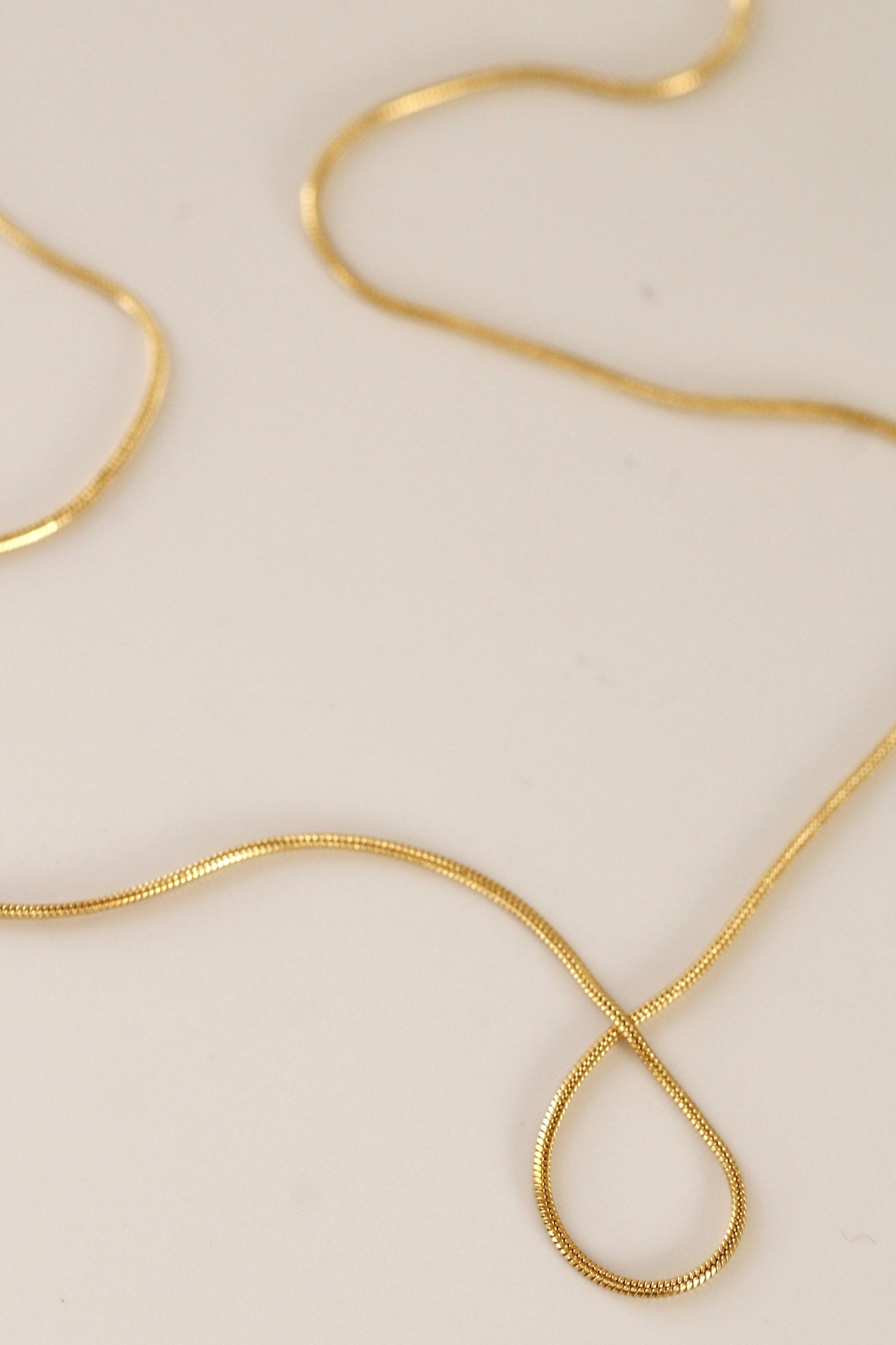 The Trail chain necklace, crafted in gold filled material, lies in gentle curves on a smooth surface—an ideal minimalist piece for everyday wear.