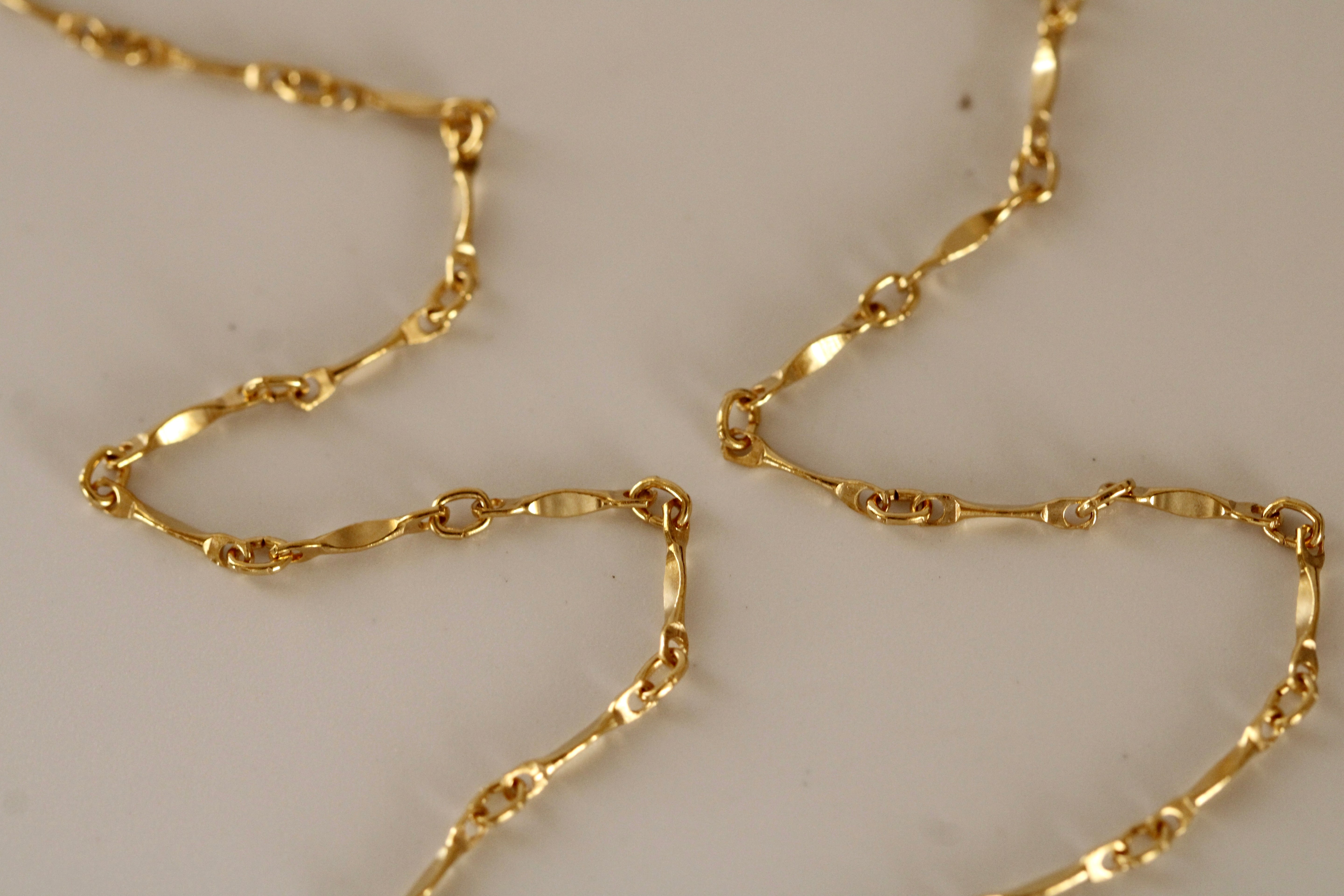 Close-up of the Twisted Link Necklace, a delicate gold-filled piece with twisted oval links arranged in a wavy pattern on a light surface—a perfect minimalist accessory.