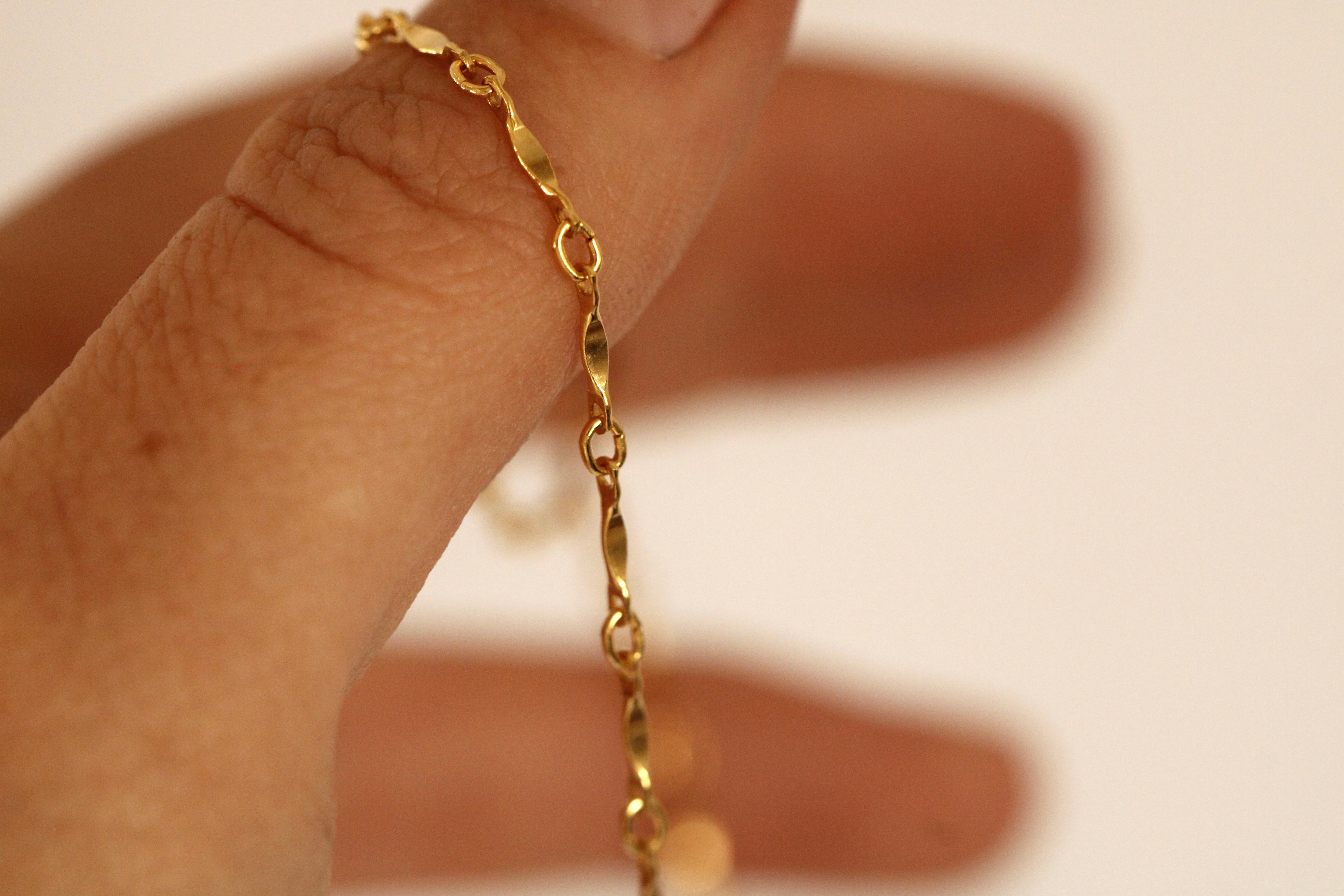 A close-up of a hand holding the Twisted Link Necklace, a delicate gold-filled piece, against a soft, neutral background.